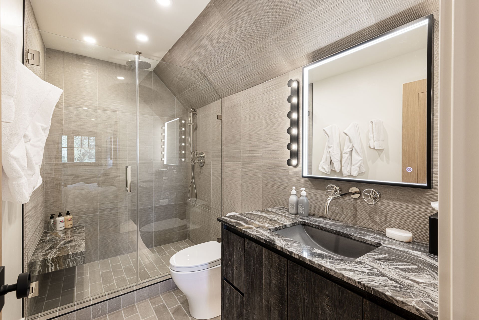 Sun Peak Manor House - Guest Bedroom 5 en suite stone counter vanity with lighted mirror and shower with a stone bench Sun Peak Manor House - Guest Bedroom 5 en suite stone counter vanity with lighted mirror and shower with a stone bench
